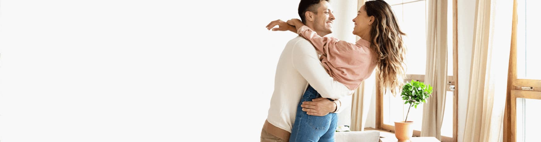 Happy young couple celebrating together at home, smiling and embracing near a bright window.