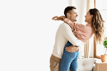 Happy young couple celebrating together at home, smiling and embracing near a bright window.