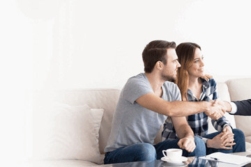 A mortgage broker shaking hands with a smiling couple in a bright living room after a successful home loan consultation.